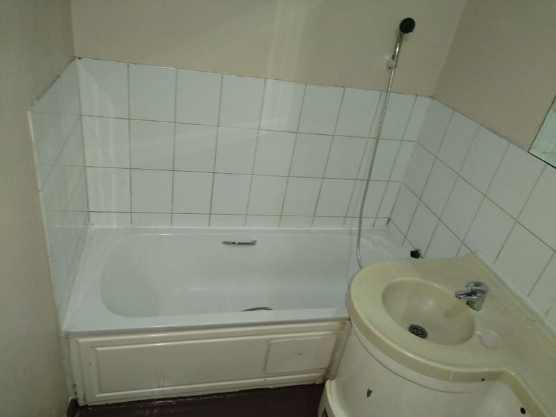 A compact bathroom featuring a standard bathtub with handheld shower attachment and a vanity basin with tiled splashback.