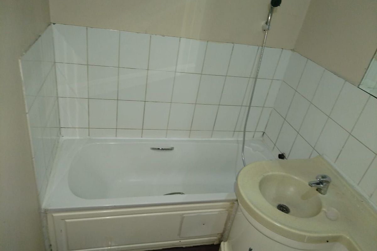 A compact bathroom featuring a standard bathtub with handheld shower attachment and a vanity basin with tiled splashback.