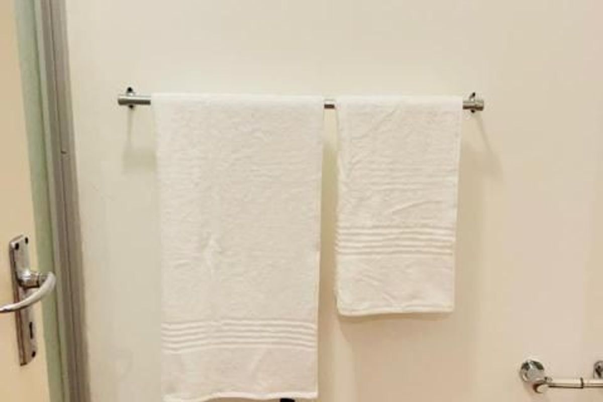 A simple bathroom wall featuring a metal towel rail and door frame, showing signs of wear at the base of the wall.