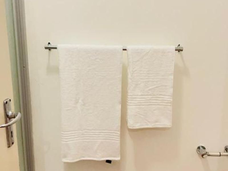 A simple bathroom wall featuring a metal towel rail and door frame, showing signs of wear at the base of the wall.