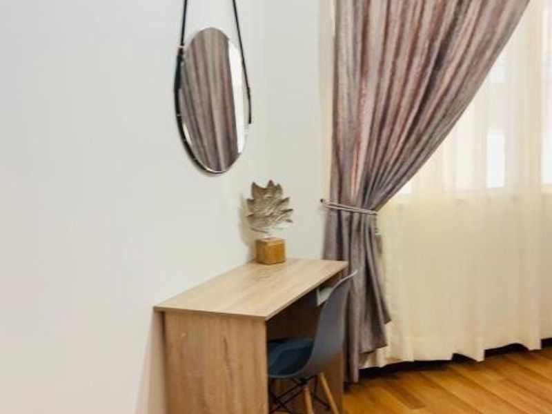 A bedroom corner featuring warm-toned laminate flooring and floor-to-ceiling curtains, providing a neutral and functional space.