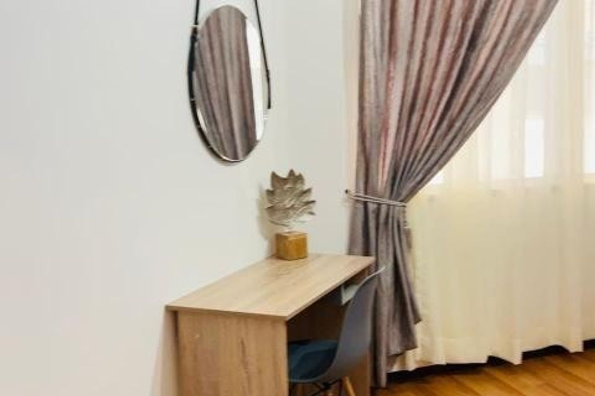 A bedroom corner featuring warm-toned laminate flooring and floor-to-ceiling curtains, providing a neutral and functional space.
