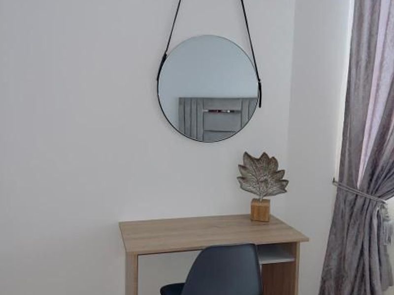 A bedroom corner featuring laminate flooring and neutral wall finishes, suitable for use as a study or vanity area.
