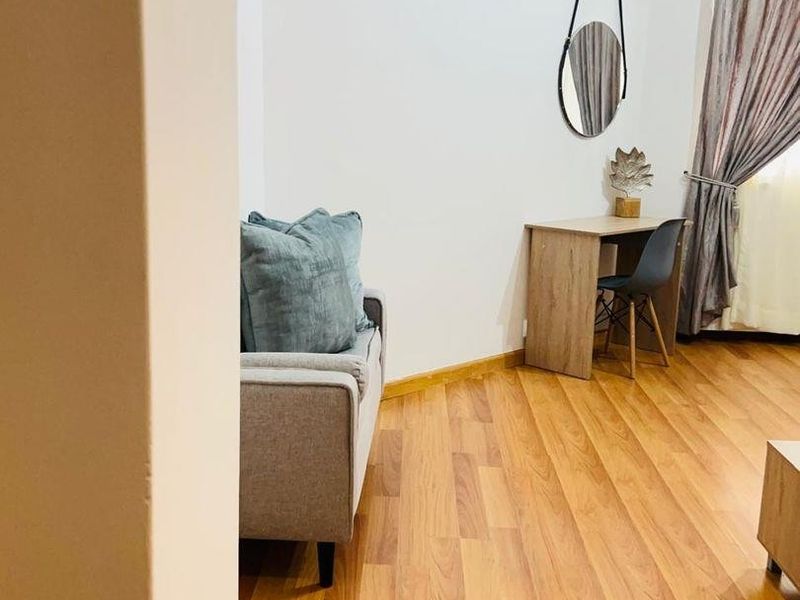 A living area featuring warm-toned laminate flooring and neutral walls, providing a functional space with natural light from the window.