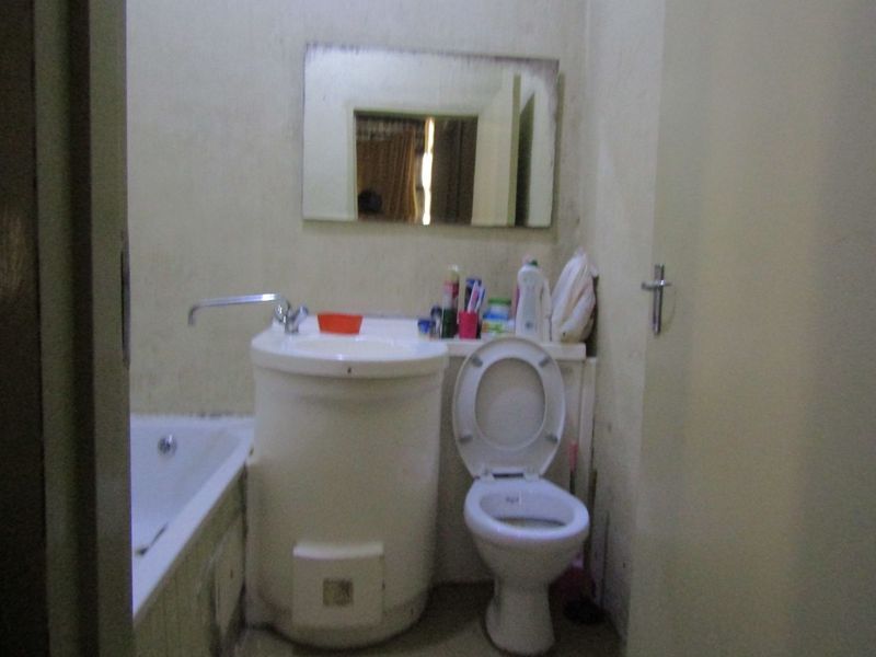 A compact bathroom featuring a standard bathtub, pedestal basin, and toilet, requiring cosmetic updates to the wall finishes and fixtures.