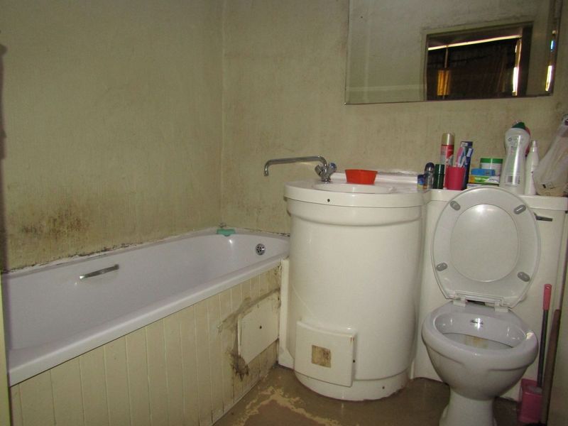 A dated bathroom featuring a standard bathtub, pedestal basin, and toilet, requiring significant cosmetic updates and repairs to wall and floor finishes.
