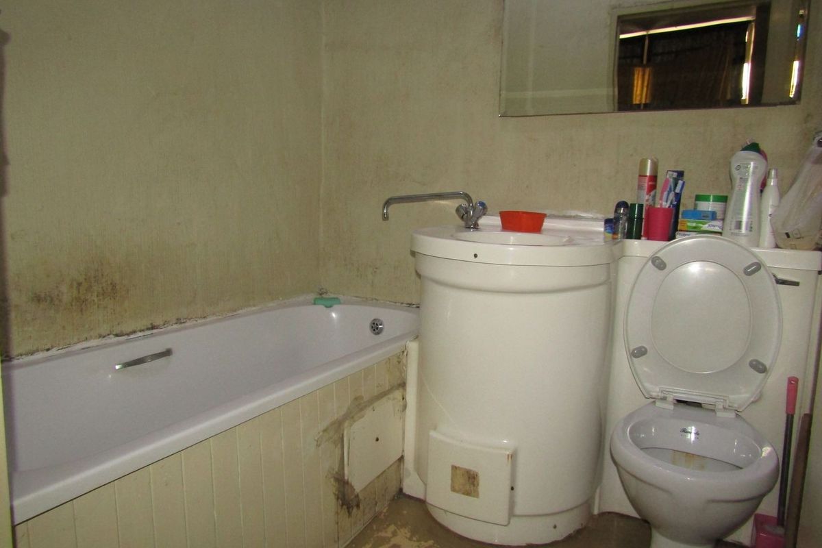 A dated bathroom featuring a standard bathtub, pedestal basin, and toilet, requiring significant cosmetic updates and repairs to wall and floor finishes.
