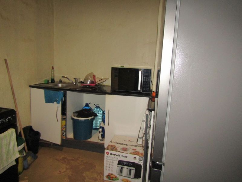A small kitchen area featuring basic base cabinetry, a sink, and a countertop, currently showing significant signs of wear and dated finishes.