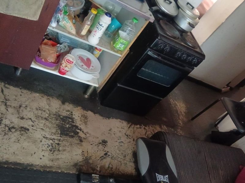 A small kitchen area featuring a freestanding stove and basic cabinetry, currently showing significant wear on the flooring surfaces.