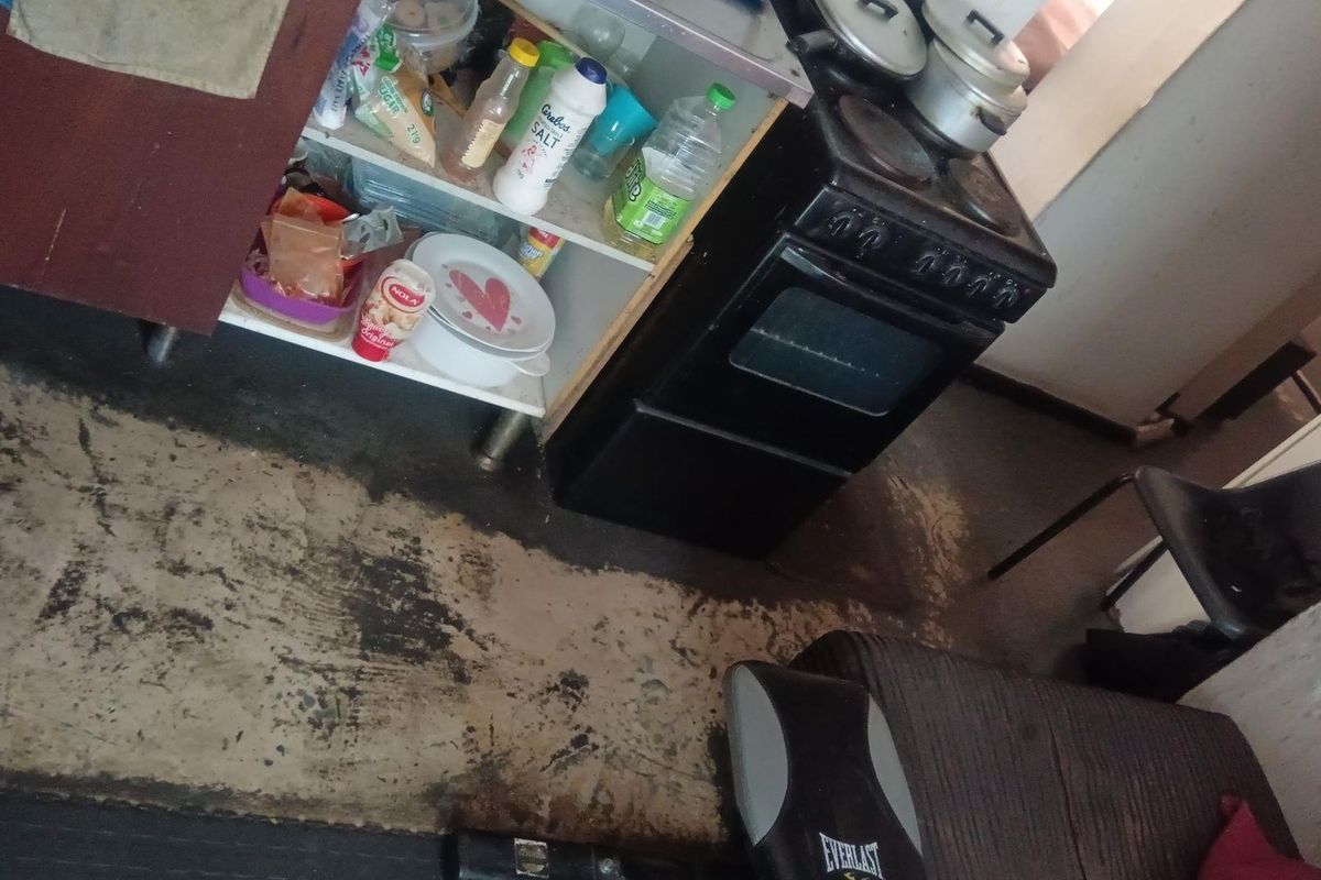 A small kitchen area featuring a freestanding stove and basic cabinetry, currently showing significant wear on the flooring surfaces.
