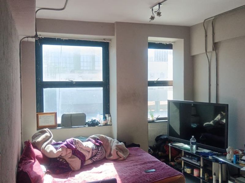 A bedroom featuring exposed electrical conduit and large casement windows, offering a functional space with potential for cosmetic updates.