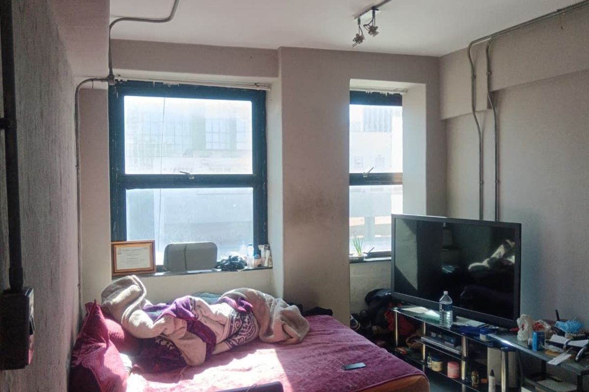 A bedroom featuring exposed electrical conduit and large casement windows, offering a functional space with potential for cosmetic updates.