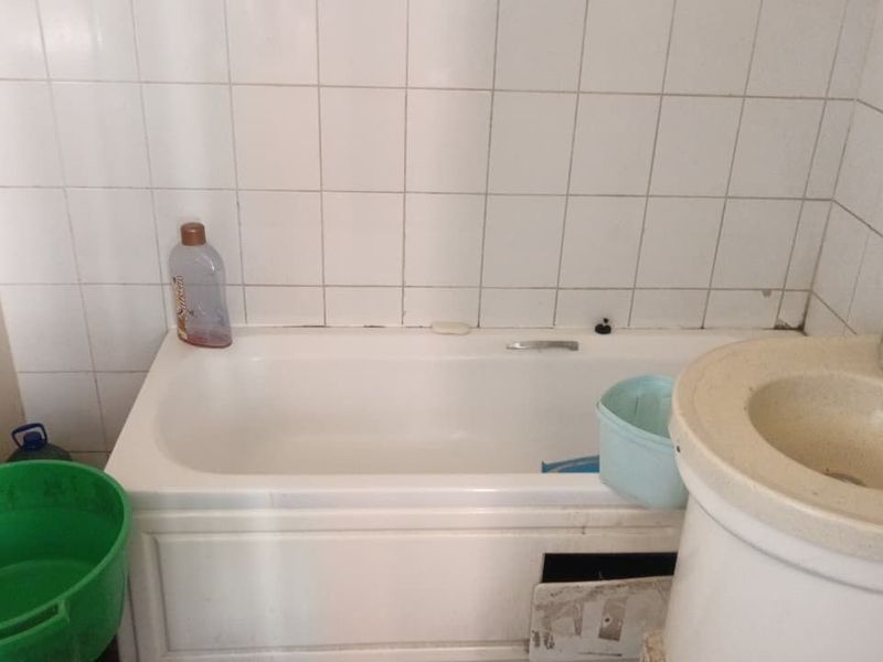 A dated bathroom featuring a standard bathtub and pedestal basin with tiled walls, requiring renovation and cosmetic updates to improve functionality and appearance.