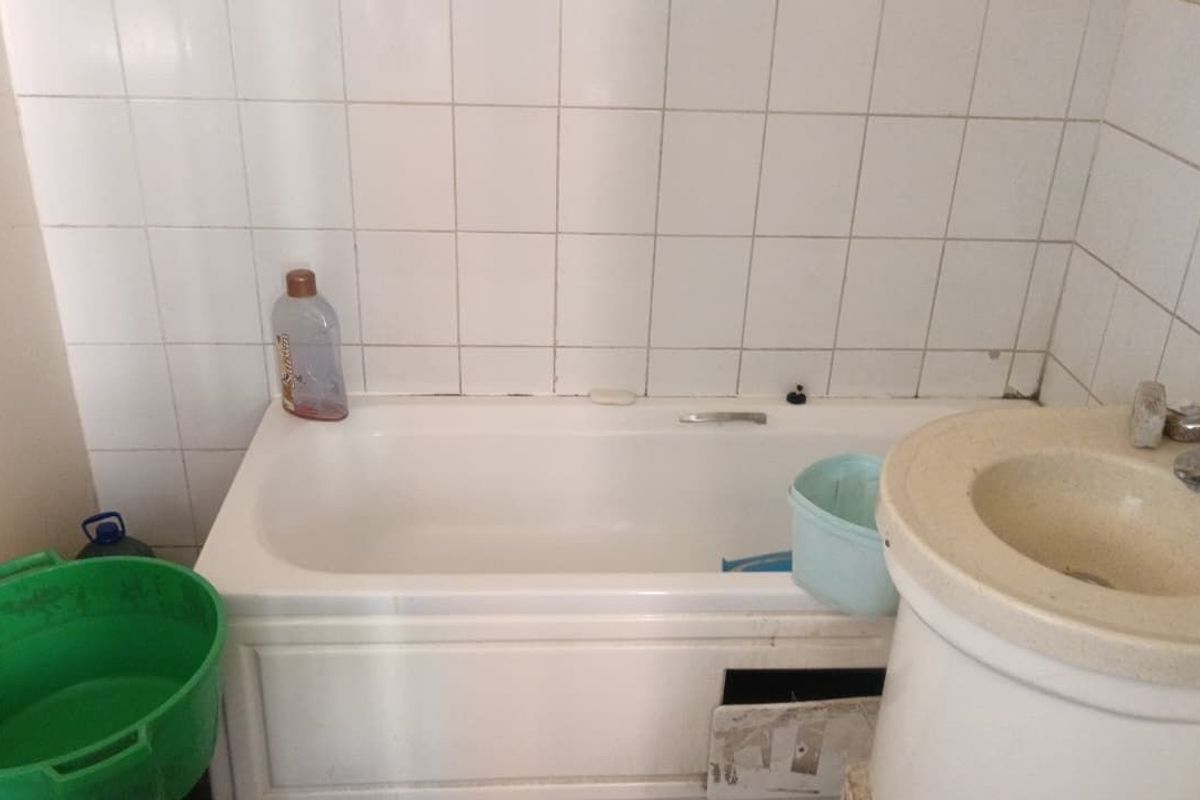 A dated bathroom featuring a standard bathtub and pedestal basin with tiled walls, requiring renovation and cosmetic updates to improve functionality and appearance.