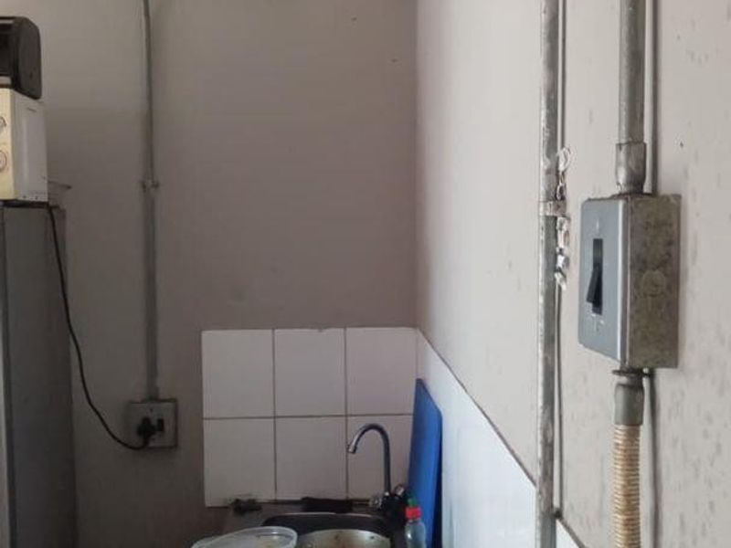 A compact kitchen area featuring a stainless steel countertop, sink, tiled splashback, and exposed electrical conduit infrastructure.