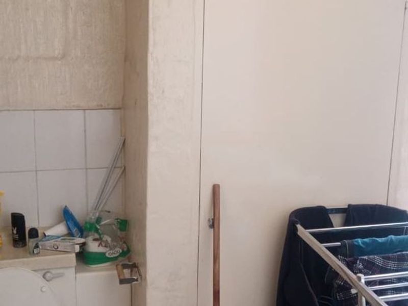 A small bathroom area featuring a toilet and tiled splashback, showing signs of wear and requiring maintenance on the wall finishes.