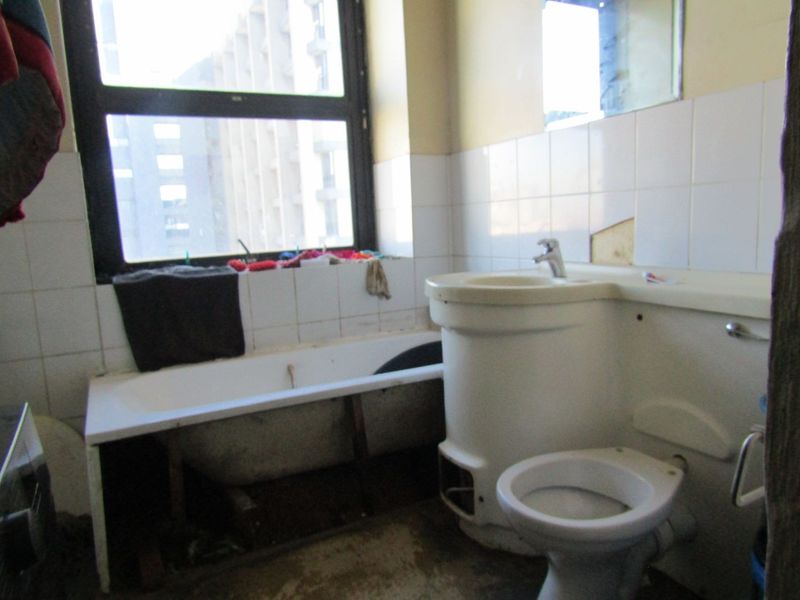 A dated bathroom featuring a bathtub, toilet, and pedestal basin with tiled splashbacks, requiring significant renovation and repair to the fixtures and finishes.