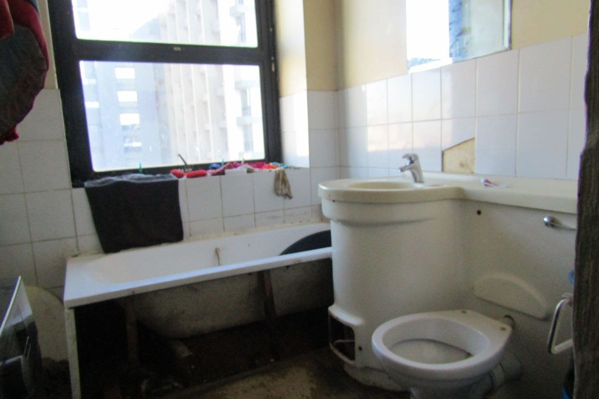 A dated bathroom featuring a bathtub, toilet, and pedestal basin with tiled splashbacks, requiring significant renovation and repair to the fixtures and finishes.