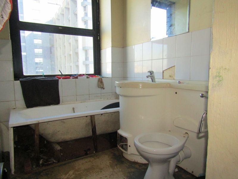 A dated bathroom featuring a bathtub, toilet, and washbasin, currently requiring significant renovation and repair to the wall tiles and overall finishes.