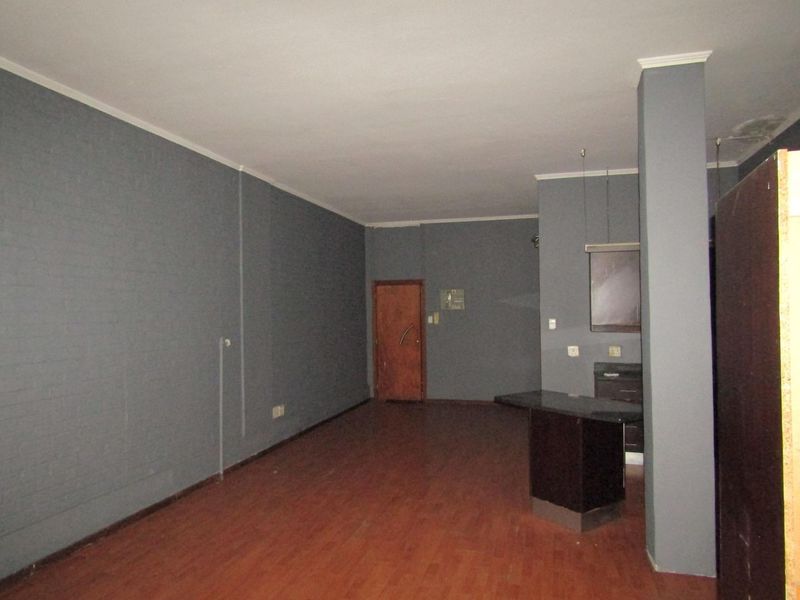 An empty open-plan living area featuring laminate flooring, a built-in breakfast counter, and a structural column, requiring minor cosmetic updates.