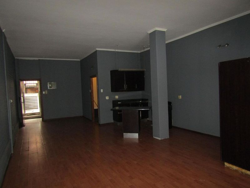 An empty open-plan living and kitchen area featuring dark cabinetry, a central structural column, and laminate wood flooring.