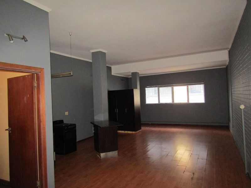 Spacious open-plan living area featuring laminate flooring, structural columns, and an exposed brick wall, offering a versatile layout for modern living.