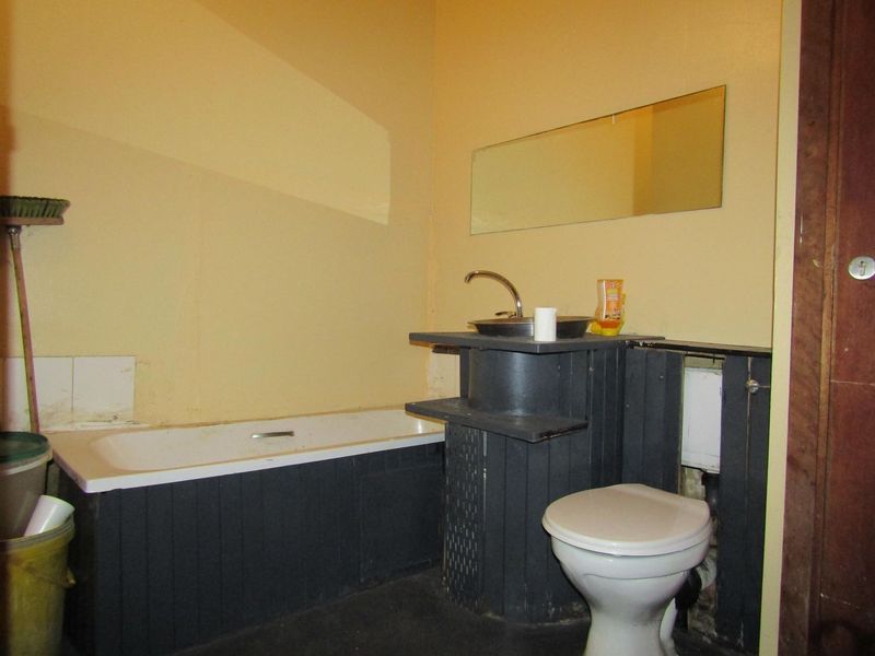 A dated bathroom featuring a bathtub, basin, and toilet with visible wear, unfinished wall surfaces, and exposed plumbing, requiring renovation and cosmetic updates.