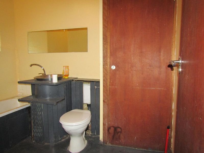 A dated bathroom featuring a basic basin, toilet, and bathtub with a wooden door and wall-mounted mirror.
