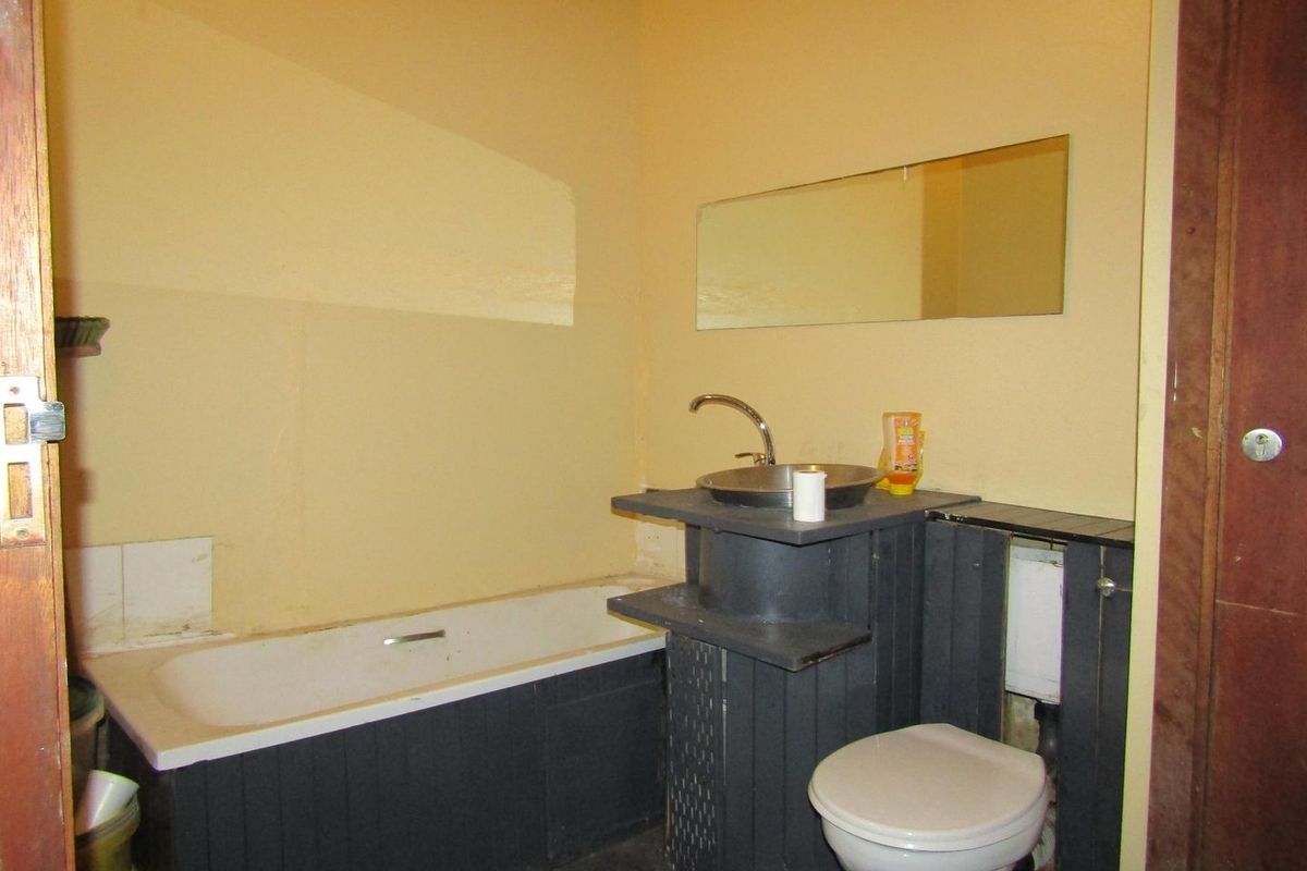 A dated bathroom featuring a bathtub, vessel sink, and toilet, requiring cosmetic updates and renovation to improve its overall condition and aesthetic appeal.