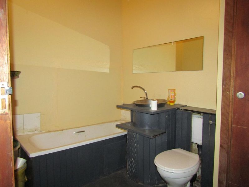 A dated bathroom featuring a bathtub, vessel sink, and toilet, requiring cosmetic updates and renovation to improve its overall condition and aesthetic appeal.
