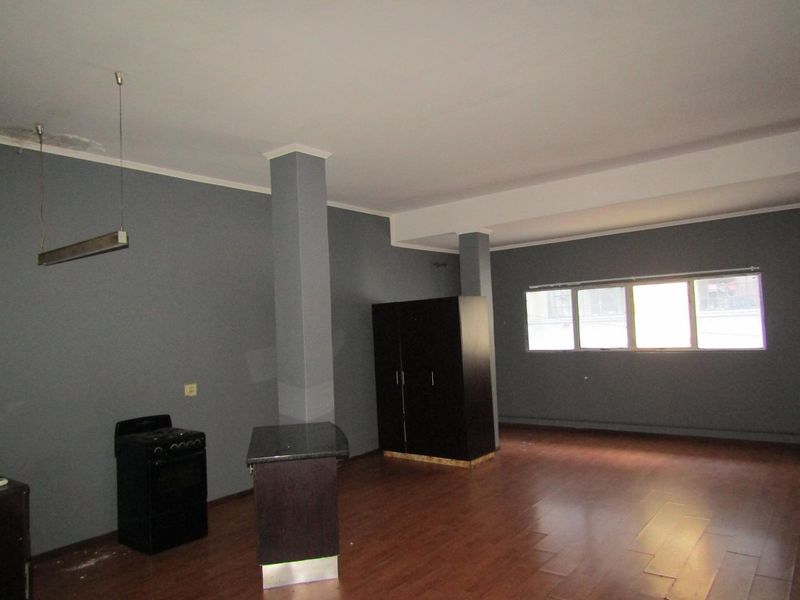 Open plan living area featuring laminate flooring, structural columns, and a basic kitchen setup with a freestanding stove.