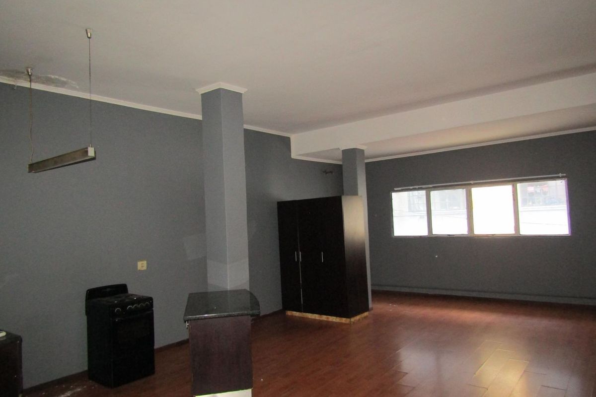 Open plan living area featuring laminate flooring, structural columns, and a basic kitchen setup with a freestanding stove.