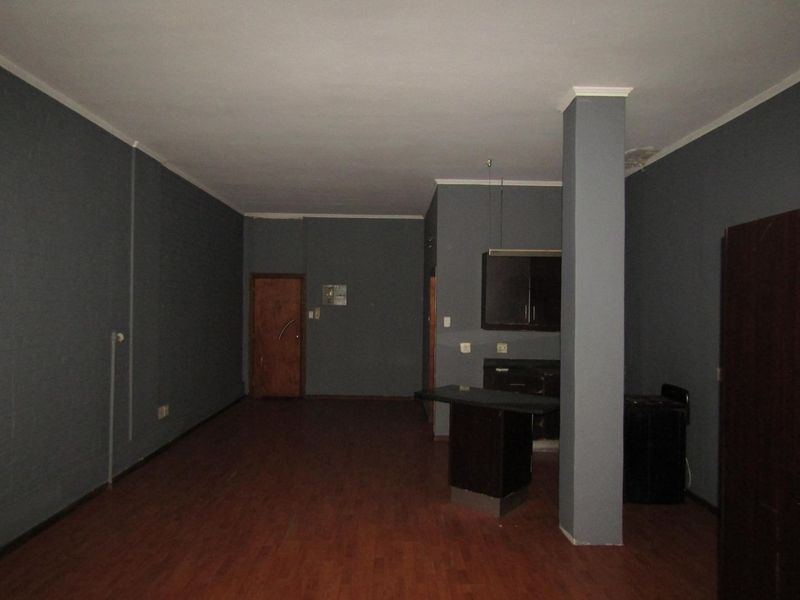 An empty open-plan living and kitchen area featuring dark cabinetry, a breakfast bar, laminate flooring, and a central structural column.
