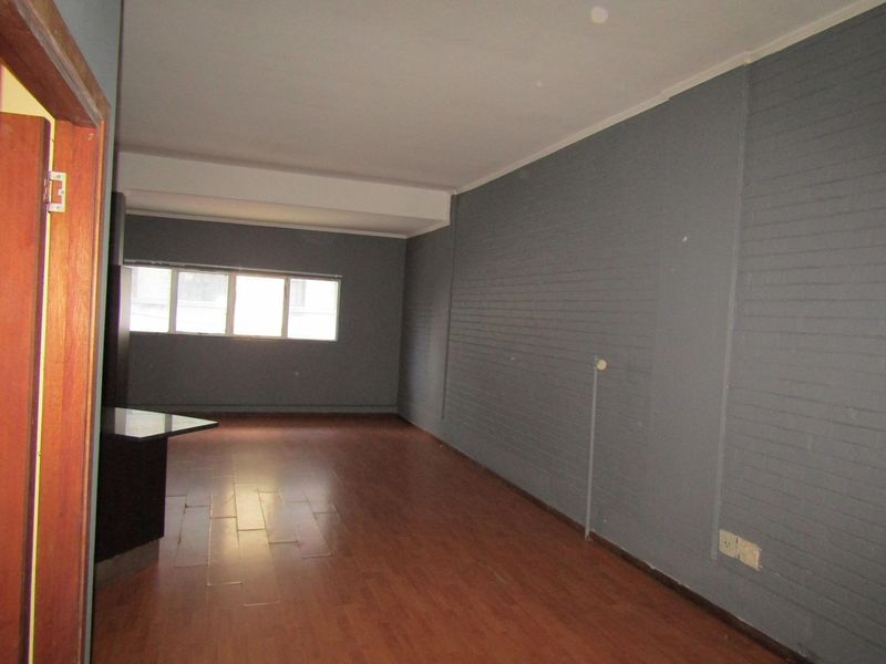An empty living area featuring laminate flooring and a painted brick feature wall, offering a blank canvas for interior design.