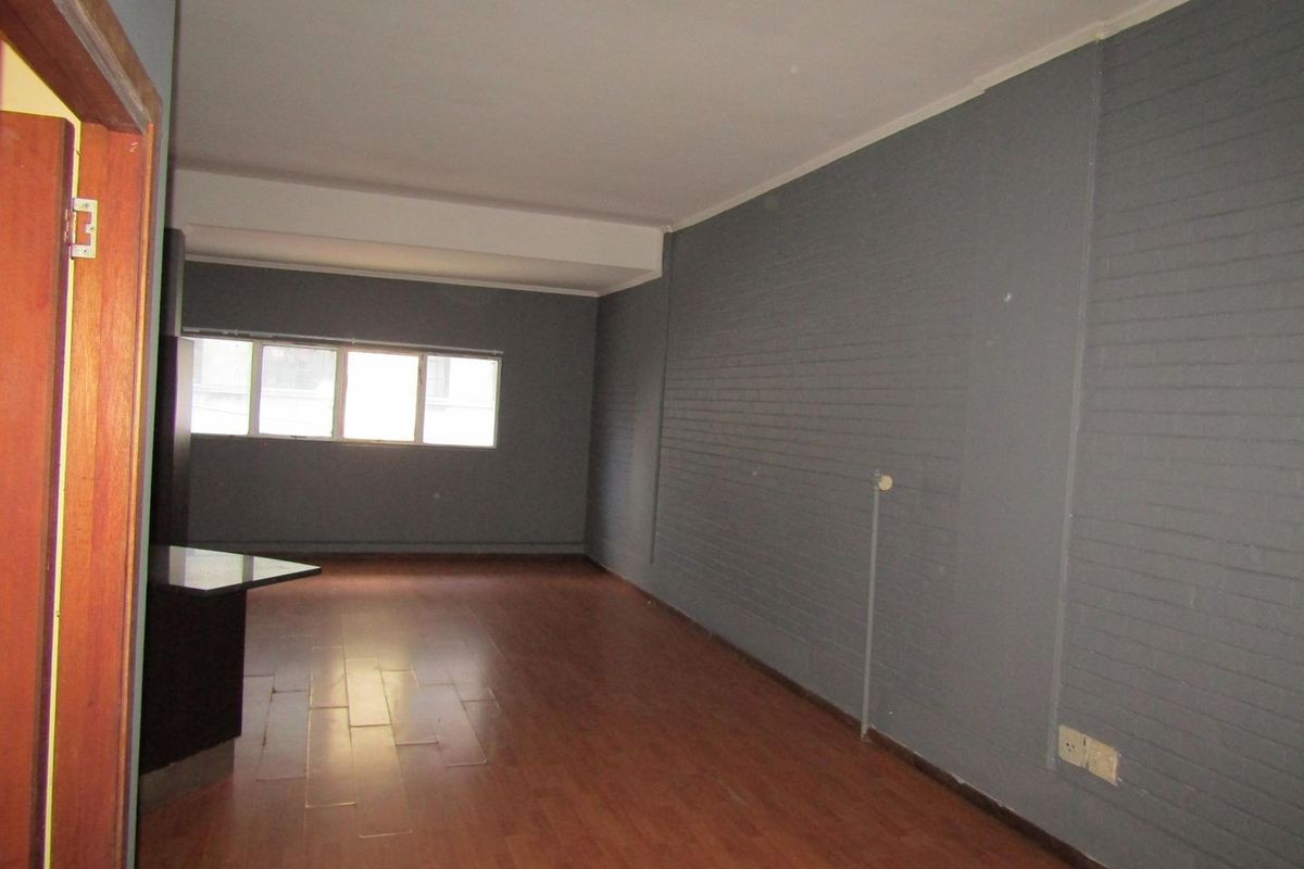 An empty living area featuring laminate flooring and a painted brick feature wall, offering a blank canvas for interior design.