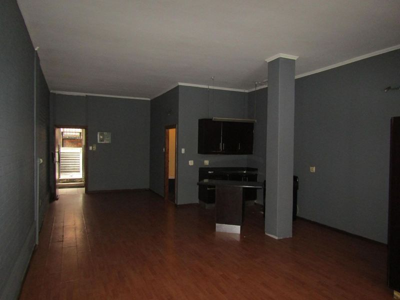 Spacious open-plan living area featuring dark grey walls, laminate flooring, a structural column, and a compact built-in kitchen unit with a breakfast bar.