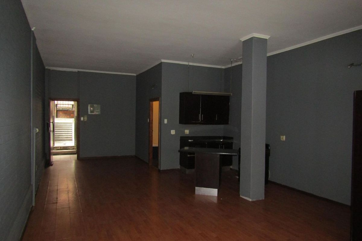 Spacious open-plan living area featuring dark grey walls, laminate flooring, a structural column, and a compact built-in kitchen unit with a breakfast bar.