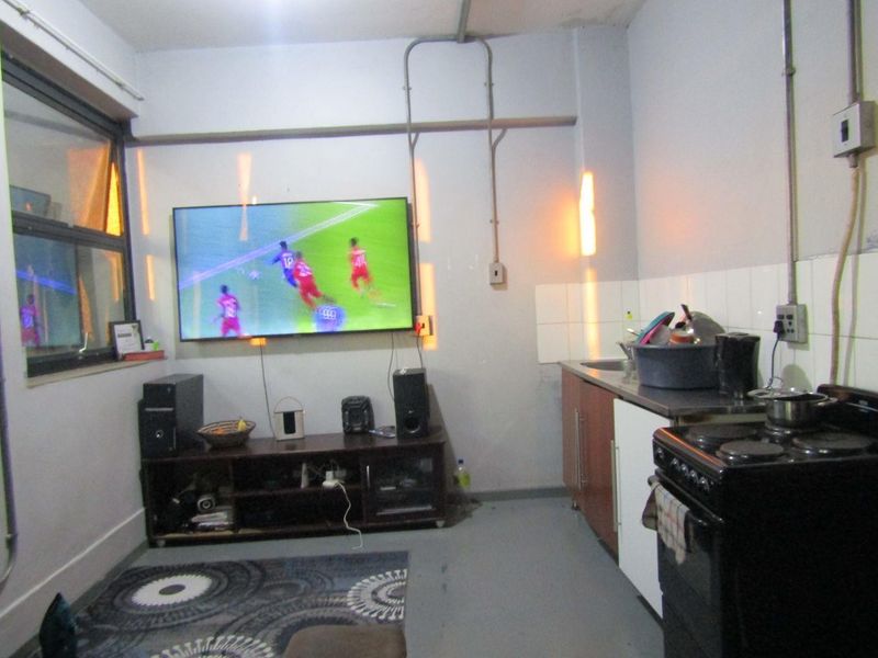 Compact open-plan living and kitchen area featuring basic cabinetry, a tiled splashback, and exposed electrical conduit, suitable for modernization.