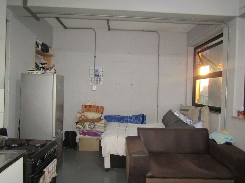 Open-plan studio apartment featuring exposed electrical conduit, industrial-style ceiling beams, and a functional kitchen area with a freestanding stove.