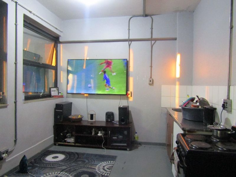 Open plan living and kitchen area featuring exposed electrical conduit, tiled backsplash, and basic kitchen fixtures in a compact apartment layout.