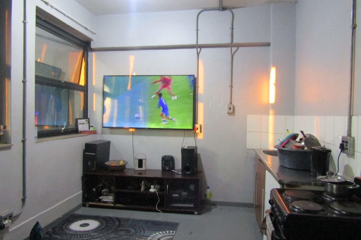 Open plan living and kitchen area featuring exposed electrical conduit, tiled backsplash, and basic kitchen fixtures in a compact apartment layout.
