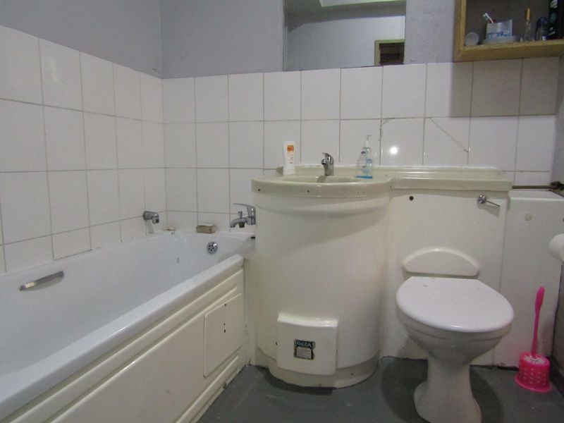 A compact bathroom featuring a combined bathtub and vanity unit with integrated basin, toilet, and wall tiling.