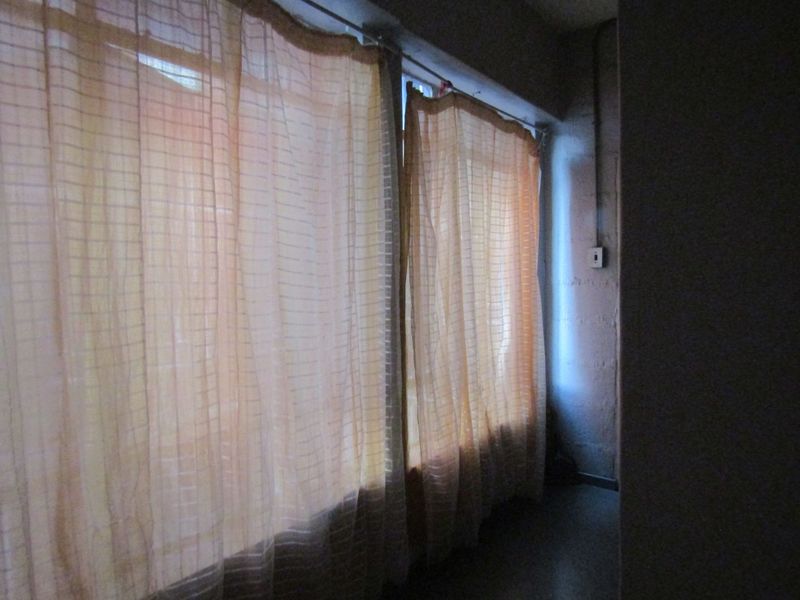 A dimly lit, sparse room featuring exposed electrical conduit and basic window treatments, requiring significant renovation to improve functionality and aesthetic appeal.