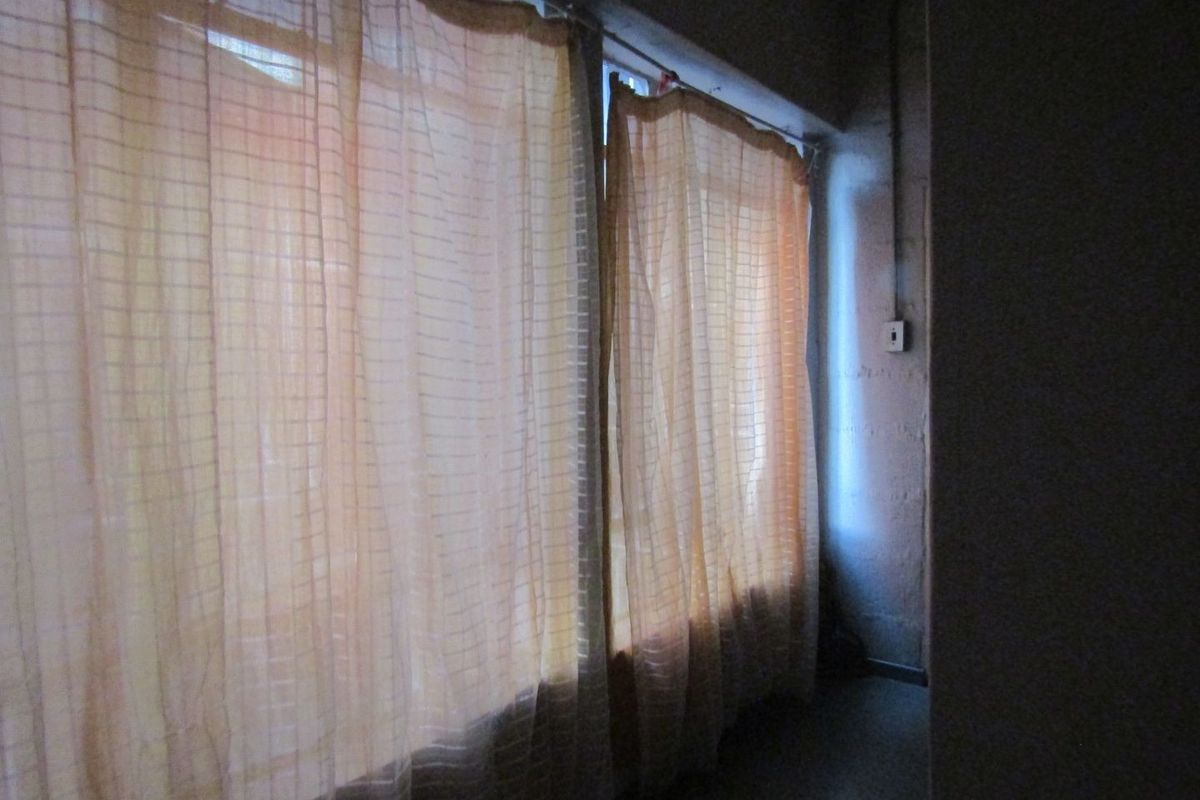 A dimly lit, sparse room featuring exposed electrical conduit and basic window treatments, requiring significant renovation to improve functionality and aesthetic appeal.