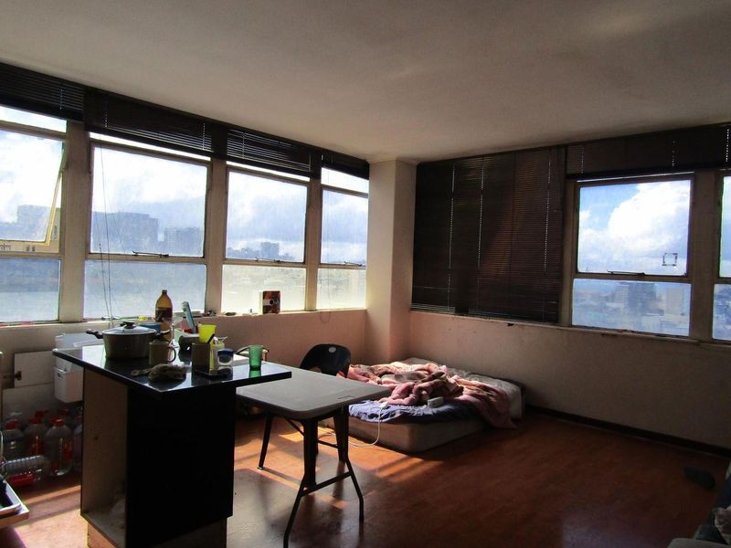 Open-plan living area featuring laminate flooring, large windows with venetian blinds, and a kitchen island, offering potential for modernization and layout optimization.