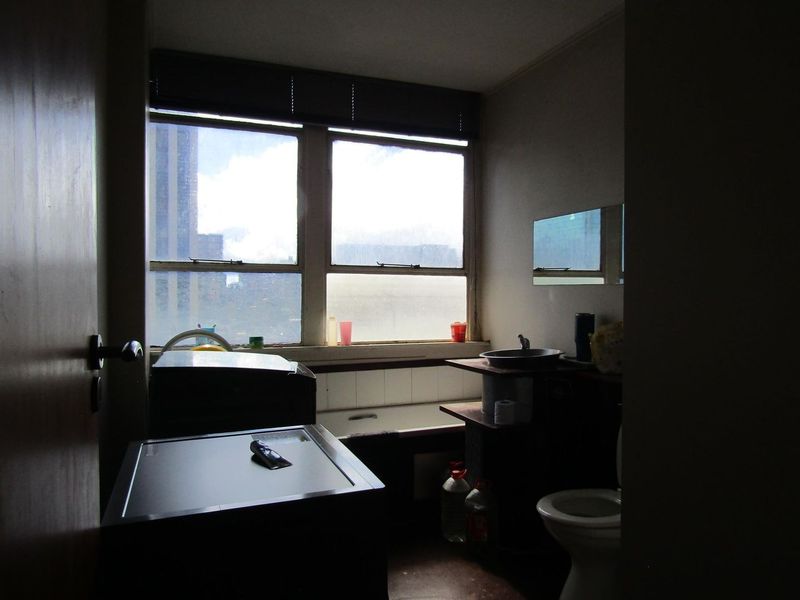 A dated bathroom featuring a bathtub, toilet, and basin, with natural light from a large window. The space would benefit from modern updates.