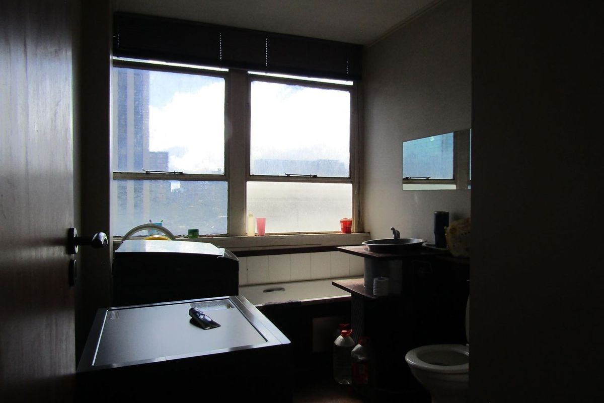 A dated bathroom featuring a bathtub, toilet, and basin, with natural light from a large window. The space would benefit from modern updates.