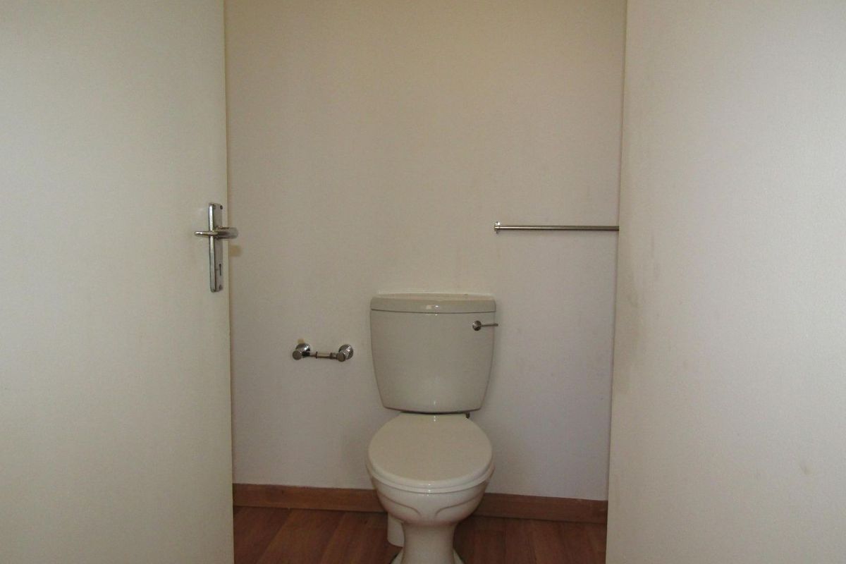 A compact, empty guest toilet featuring laminate flooring, a standard toilet suite, and wall-mounted fixtures.