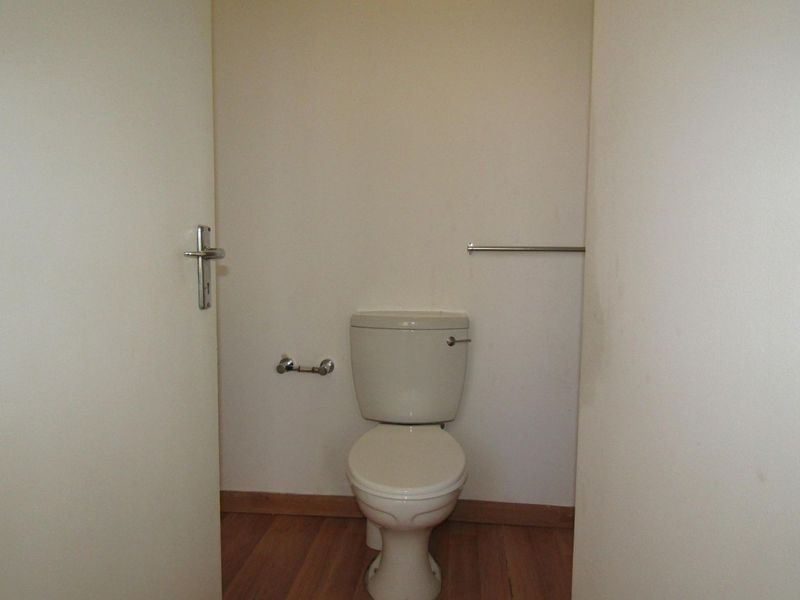 A compact, empty guest toilet featuring laminate flooring, a standard toilet suite, and wall-mounted fixtures.