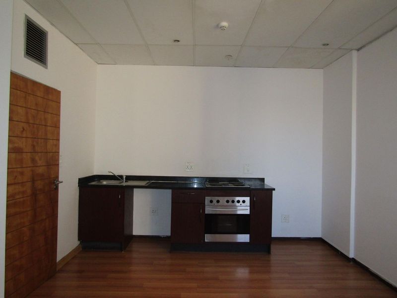 A compact, empty kitchen area featuring dark wood cabinetry, granite countertops, a built-in oven, and laminate flooring, requiring minor repairs to cabinetry.
